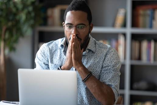 Worried man in front of computer. He has his hands together in prayer, and looks concerned. He might have "hacked from a phone, or spread after a data breach; the firm has the resources to shoulder."